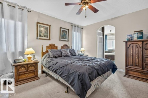 Wall-to-wall carpeted bedroom featuring an arched doorway, window with drapes, and a ceiling fan with integrated lighting - 39 Wilkinson Place, Leduc, AB 