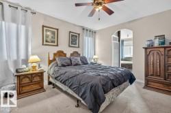 Wall-to-wall carpeted bedroom featuring an arched doorway, window with drapes, and a ceiling fan with integrated lighting - 