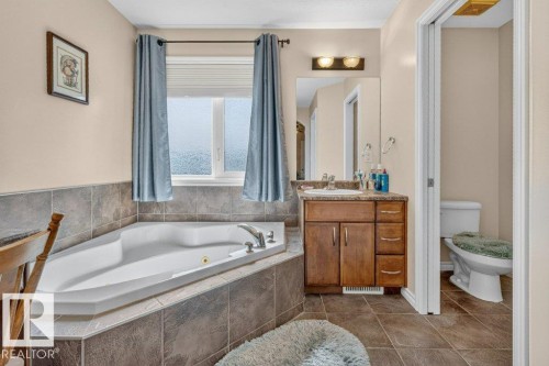 Corner soaking tub with tiled surround, wood-finish vanity with countertop, integrated sink, and wall-mounted mirror - 39 Wilkinson Place, Leduc, AB 