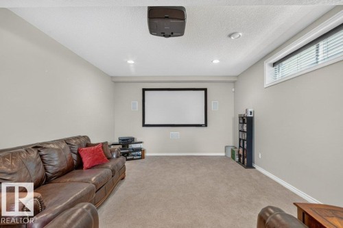 Dedicated media room featuring a large projection screen, integrated ceiling projector, built-in wall speakers, recessed lighting, and a horizontal window with blinds - 39 Wilkinson Place, Leduc, AB 