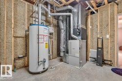 Utility room featuring a water heater, furnace, exposed wood framing, insulation, and concrete flooring - 