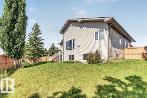 Sloped rear yard with a wooden fence and mature trees - 39 Wilkinson Place, Leduc, AB 