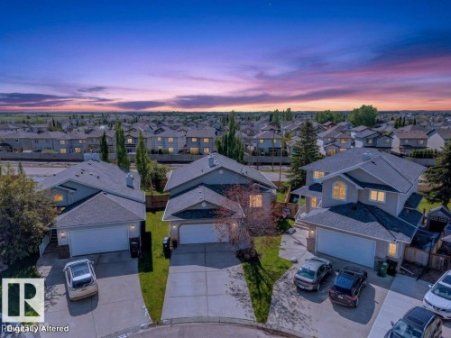 Residential streetscape featuring multiple gray-sided homes with attached garages, concrete driveways, and landscaped front yards - 39 Wilkinson Place, Leduc, AB 