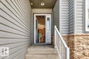 Inviting front entry featuring neutral siding, stacked stone accents, a full-lite entry door with decorative glass, and a white railing - 39 Wilkinson Place, Leduc, AB 