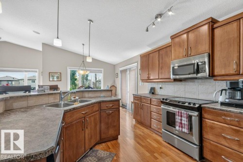 Kitchen featuring wood-finish cabinetry, stainless steel appliances, a double basin sink, and wood-finish flooring - 39 Wilkinson Place, Leduc, AB 