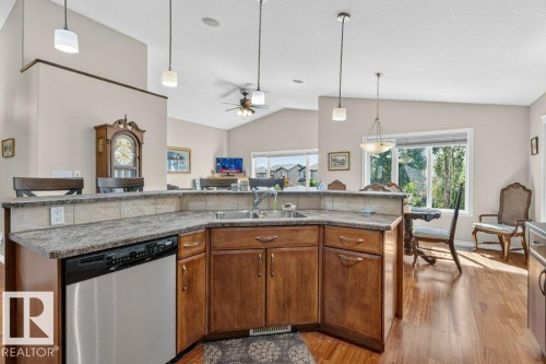 Spacious kitchen featuring wood cabinetry, stainless steel dishwasher, and a stone-finish countertop with an integrated sink - 39 Wilkinson Place, Leduc, AB 