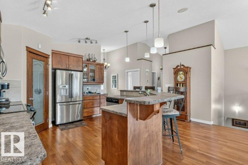 Spacious kitchen featuring a large island with seating, stainless steel appliances, abundant wood cabinetry, and wood-finish flooring - 39 Wilkinson Place, Leduc, AB 