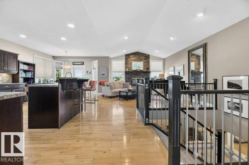Open-concept living area featuring light wood-finish flooring, a kitchen island with seating, a stone fireplace, vaulted ceilings, and a staircase with metal balusters - 5528 43 Street, Lamont, AB 