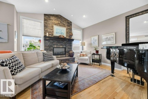Living area featuring a stone accent wall with a built-in fireplace, vaulted ceilings, and wood-finish flooring - 5528 43 Street, Lamont, AB 