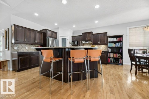 Spacious kitchen featuring an island with a breakfast bar, dark wood cabinetry, a tiled backsplash, stainless steel appliances, and light wood-finish flooring - 5528 43 Street, Lamont, AB 