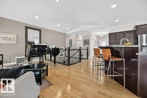 Open-concept living area featuring light wood-finish flooring, recessed lighting, a built-in kitchen island with a stone countertop, and dark wood cabinetry - 5528 43 Street, Lamont, AB 