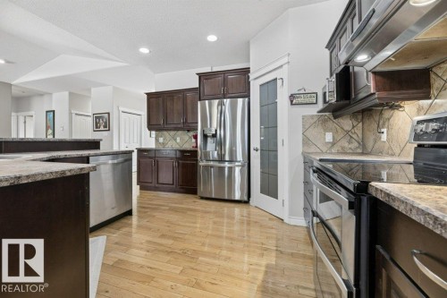 Kitchen featuring wood-finish flooring, dark wood cabinetry, stainless steel appliances, and a tiled backsplash - 5528 43 Street, Lamont, AB 