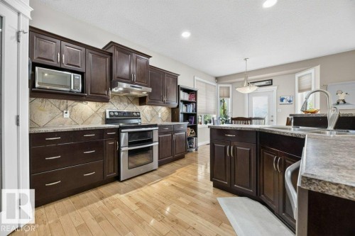 Contemporary kitchen featuring dark wood cabinetry, light wood-finish flooring, stainless steel appliances, and stone countertops - 5528 43 Street, Lamont, AB 