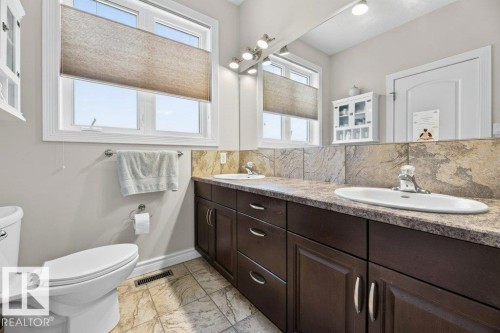 Bathroom featuring dual windows, a double vanity with dark wood-finish cabinetry, a stone-look countertop, and a tiled floor - 5528 43 Street, Lamont, AB 
