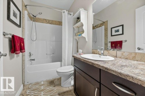 Bathroom featuring a tub/shower combination with tile surround, a dark wood-finish vanity with a light-toned countertop, and an integrated sink with a chrome faucet - 5528 43 Street, Lamont, AB 