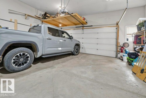 Spacious garage featuring a concrete floor, overhead shelving, and a large white overhead door - 5528 43 Street, Lamont, AB 