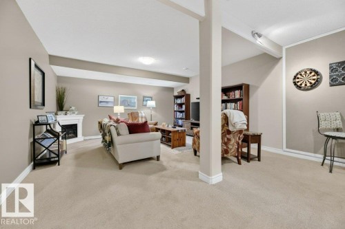 Carpeted recreation room featuring a corner fireplace with a white mantel, neutral wall paint, white baseboards, and overhead lighting - 5528 43 Street, Lamont, AB 