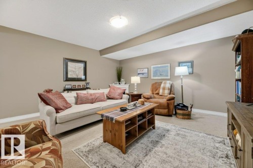 Carpeted living area featuring a neutral color palette, ceiling-mounted light fixture, and a built-in architectural beam - 5528 43 Street, Lamont, AB 