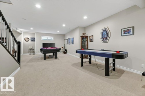 Spacious recreation area featuring light-toned carpeting, recessed ceiling lighting, a dark wood staircase with black balusters, and a window providing natural light - 5528 43 Street, Lamont, AB 