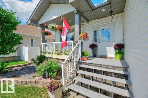 Inviting front porch featuring a white vinyl railing, stone veneer accents, and a panel door with decorative glass - 5528 43 Street, Lamont, AB 