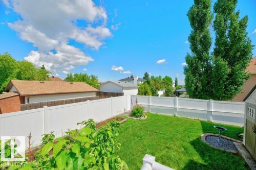 Expansive backyard featuring a lush green lawn, mature perimeter trees, and a full privacy fence - 5528 43 Street, Lamont, AB 