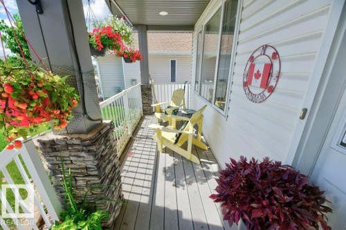 Covered front porch featuring stacked stone pillar accents, composite decking, white railing, and multiple windows - 5528 43 Street, Lamont, AB 