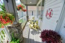 Covered front porch featuring stacked stone pillar accents, composite decking, white railing, and multiple windows - 5528 43 Street, Lamont, AB 