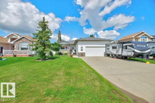 Single-story property featuring a white exterior with stone accents, an attached garage, a paved driveway, and a manicured front lawn - 5528 43 Street, Lamont, AB 