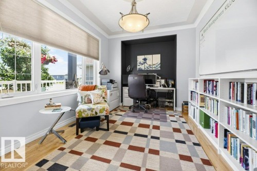 Bright room featuring extensive natural light from a large window with roller shades, wood-finish flooring, a built-in office alcove, an overhead semi-flush mount light fixture, and built-in shelving - 5528 43 Street, Lamont, AB 