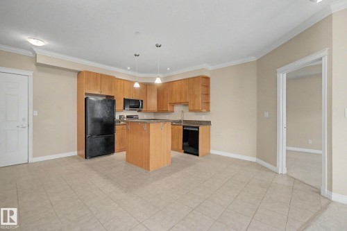 Kitchen featuring warm wood cabinetry, dark countertops, and black appliances - 413 10116 80 Avenue, Edmonton, AB 