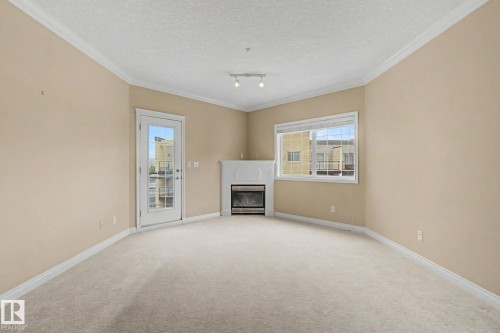 Carpeted living space featuring a corner fireplace with a white mantel, a glass-paned door, and a multi-pane window - 413 10116 80 Avenue, Edmonton, AB 