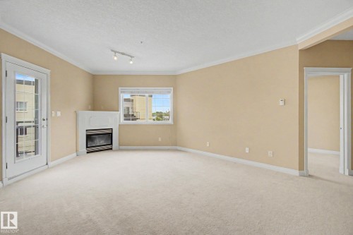 Spacious interior featuring a built-in fireplace with a white mantel, beige wall paint, white trim, recessed lighting, and an exterior door with glass panels - 413 10116 80 Avenue, Edmonton, AB 