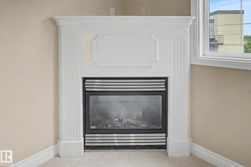 White corner fireplace with decorative mantel, black glass-front insert, and detailed fluted pillars - 413 10116 80 Avenue, Edmonton, AB 
