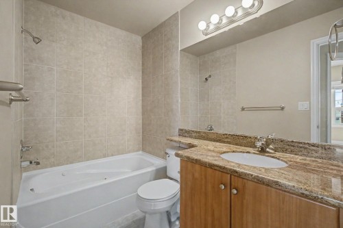 Bathroom featuring a built-in tub with shower, neutral wall tile surround, and a vanity with a stone countertop and integrated sink - 413 10116 80 Avenue, Edmonton, AB 