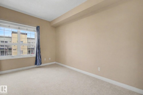 Carpeted room with a multi-pane window, light beige wall paint, white baseboards, and a dropped ceiling feature - 413 10116 80 Avenue, Edmonton, AB 