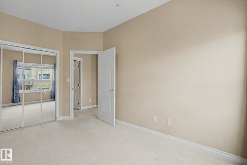 Bedroom with neutral carpeting, light-colored walls, white baseboards, and a mirrored sliding closet door - 413 10116 80 Avenue, Edmonton, AB 