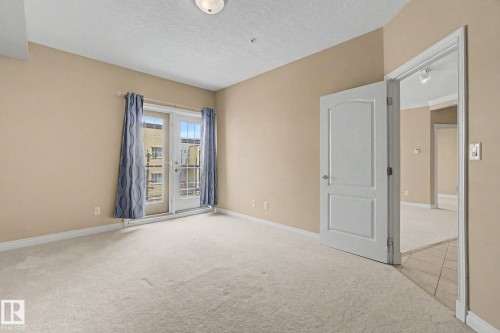 Room featuring light neutral carpeting, a white paneled door, and trim - 413 10116 80 Avenue, Edmonton, AB 
