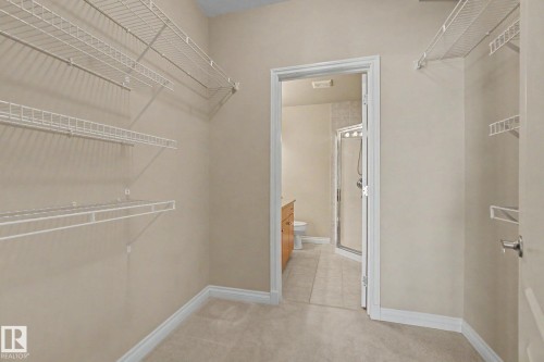 Walk-in closet with carpet flooring, white wire shelving, and a doorway opening to a bathroom featuring a glass-enclosed shower, a wood-finish vanity, and light-toned tile flooring - 413 10116 80 Avenue, Edmonton, AB 