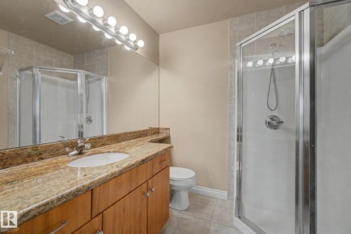 Bathroom featuring a granite countertop vanity with wood cabinetry, an undermount sink, and a mirrored wall - 413 10116 80 Avenue, Edmonton, AB 