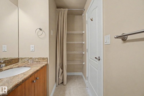 Bathroom vanity featuring a vessel sink, stone-finish countertop, wood-finish cabinetry, and built-in shelving - 413 10116 80 Avenue, Edmonton, AB 