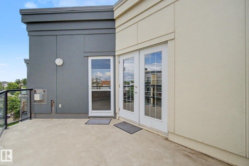 Spacious concrete balcony with glass railing, providing direct exterior access via a white single-panel door and white French doors - 413 10116 80 Avenue, Edmonton, AB 