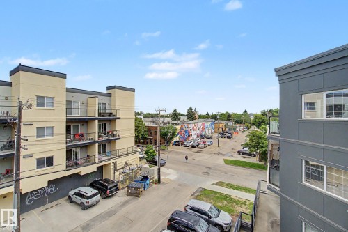 Urban streetscape featuring a multi-story building with balconies, a neighboring building with modern grey siding, and a distant building with a colorful mural - 413 10116 80 Avenue, Edmonton, AB 