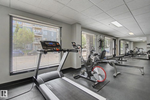 Fitness room featuring resilient rubber flooring, expansive windows with horizontal blinds, built-in mirror, and recessed lighting fixtures - 413 10116 80 Avenue, Edmonton, AB 