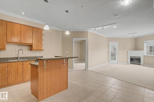 Open-concept living space featuring a kitchen with wood cabinetry and stone-finish countertops, a breakfast bar, and pendant lighting - 413 10116 80 Avenue, Edmonton, AB 