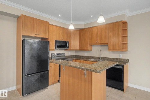 Kitchen featuring wood-finish cabinetry, granite-style countertops, stainless steel sink, black appliances, and pendant lighting - 413 10116 80 Avenue, Edmonton, AB 