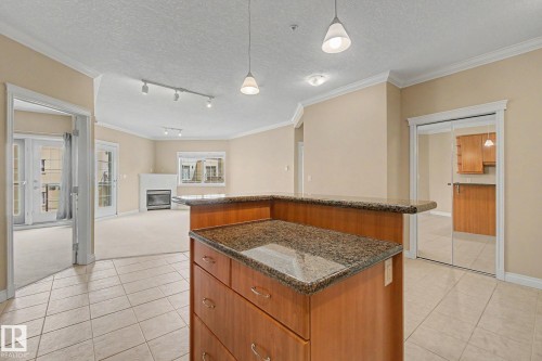 Kitchen island with granite-finish countertop and integrated drawers, complemented by pendant lighting - 413 10116 80 Avenue, Edmonton, AB 