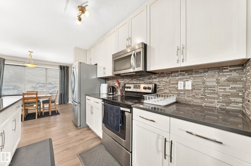 Kitchen featuring white cabinetry, stainless steel appliances, dark countertops, and a mosaic tile backsplash - 875 Chappelle Link Link, Edmonton, AB 