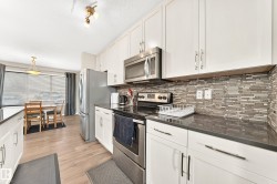 Kitchen featuring white cabinetry, stainless steel appliances, dark countertops, and a mosaic tile backsplash - 