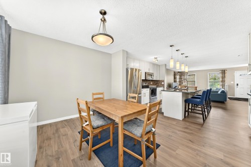 Open-concept interior featuring wood-finish flooring, a kitchen island with pendant lighting, stainless steel appliances, and light-toned cabinetry - 875 Chappelle Link Link, Edmonton, AB 