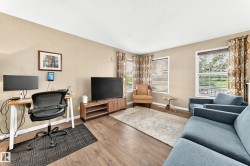 Spacious living area featuring wood-finish flooring, neutral wall tones, and multiple windows with blinds - 
